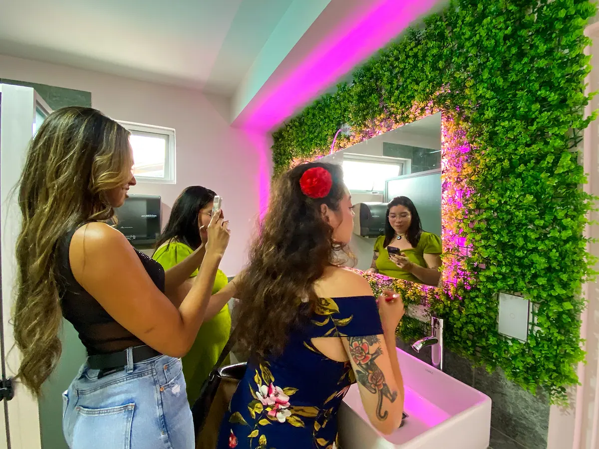 Three guests getting ready together at the plant-framed mirror with pink light