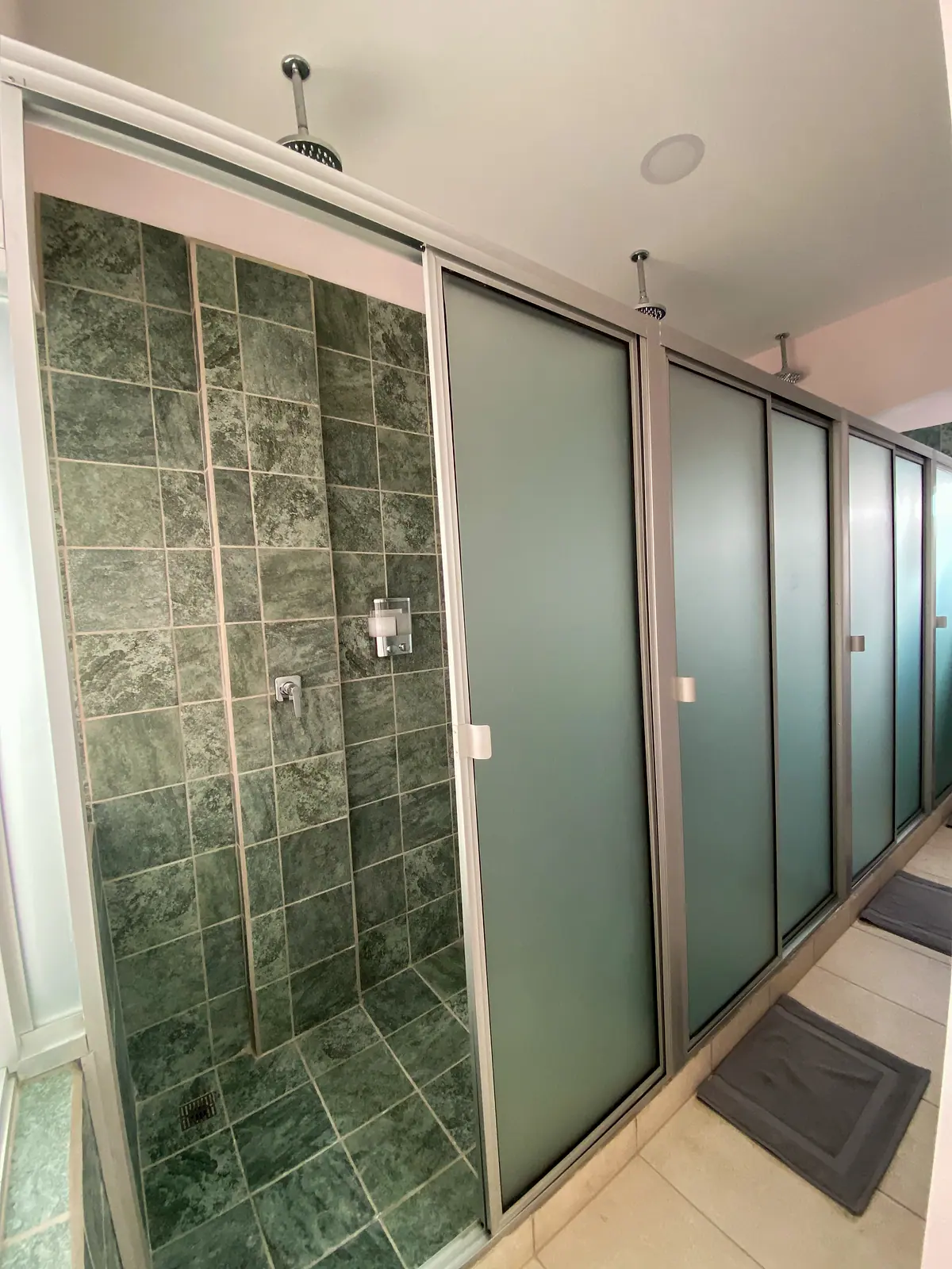 A row of private shower stalls with frosted doors and green stone walls