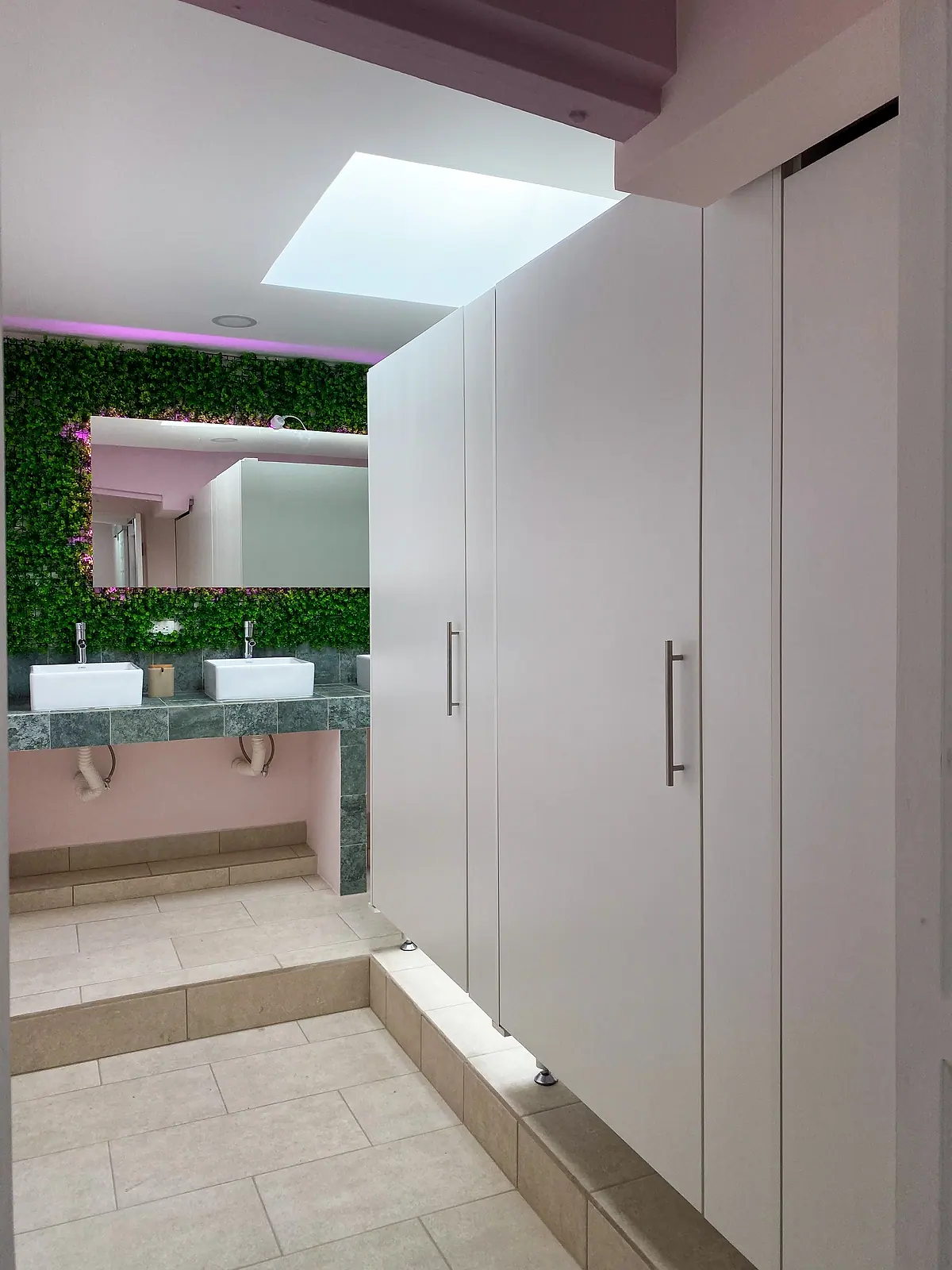 Double-basin vanity under a plant wall next to tall white cabinets