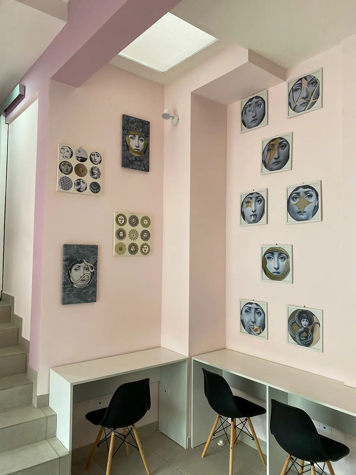 The work corner: white desks and black chairs under the stairs, with face-plate art on the wall