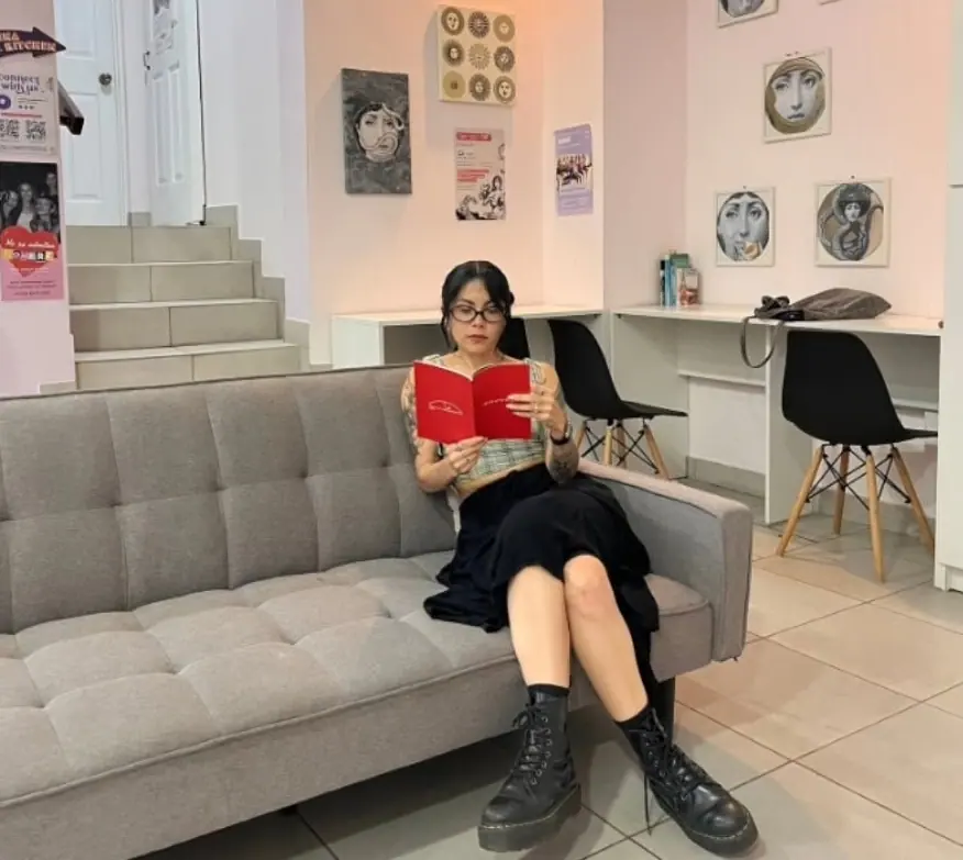 A guest reading on the lounge sofa next to the white work desks and black chairs of the coworking corner