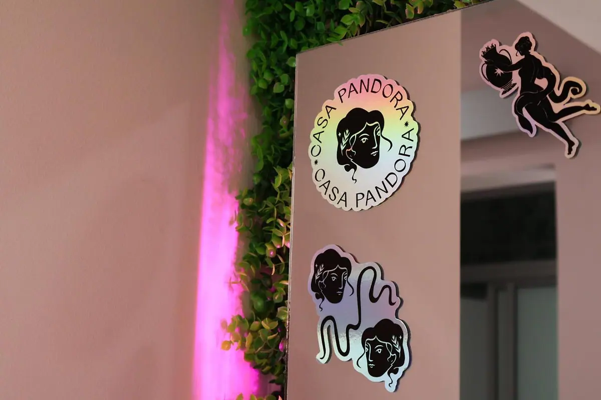 Casa Pandora face stickers on a cabinet next to the plant wall and its pink neon