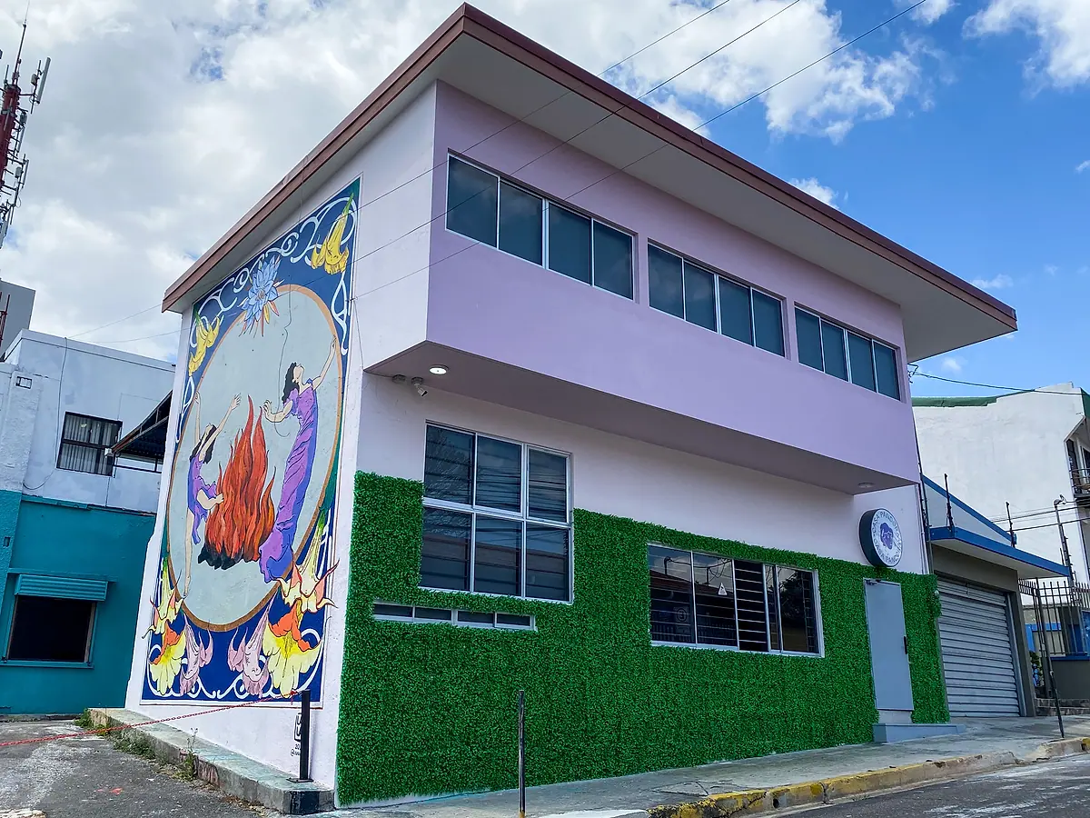 Casa Pandora from the street: lilac upper floor, a green living wall and the side mural of two women dancing around a fire