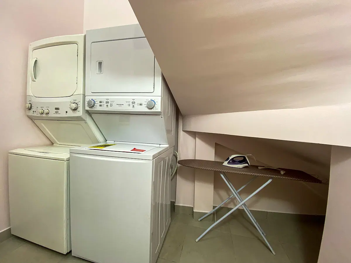 Laundry room with two stacked washer-dryer towers and an ironing board