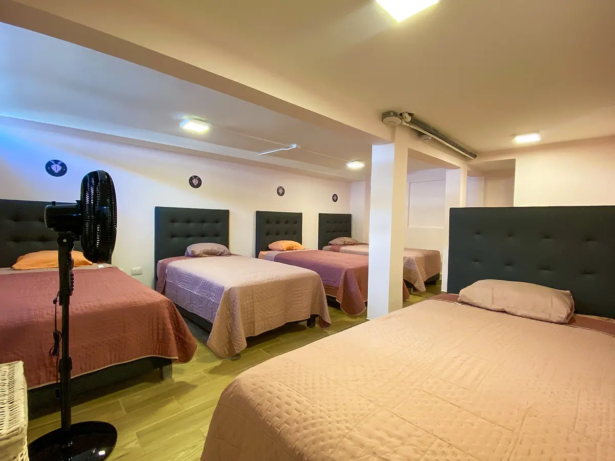 Vasija dorm: single beds in a row, each with a padded dark headboard, and a standing fan